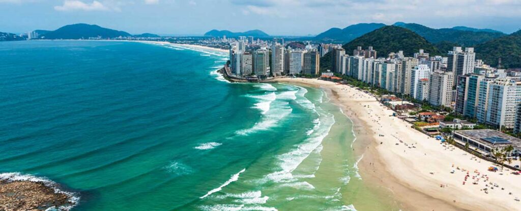 Descubra a magia de viajar de ônibus para o litoral Visão aérea do mar e de uma praia com prédios da cidade à esquerda.