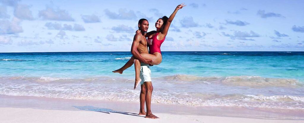 Viajar a dois para a praia pode render momentos românticos e de diversão. Casal de homem e mulher negros na praia.