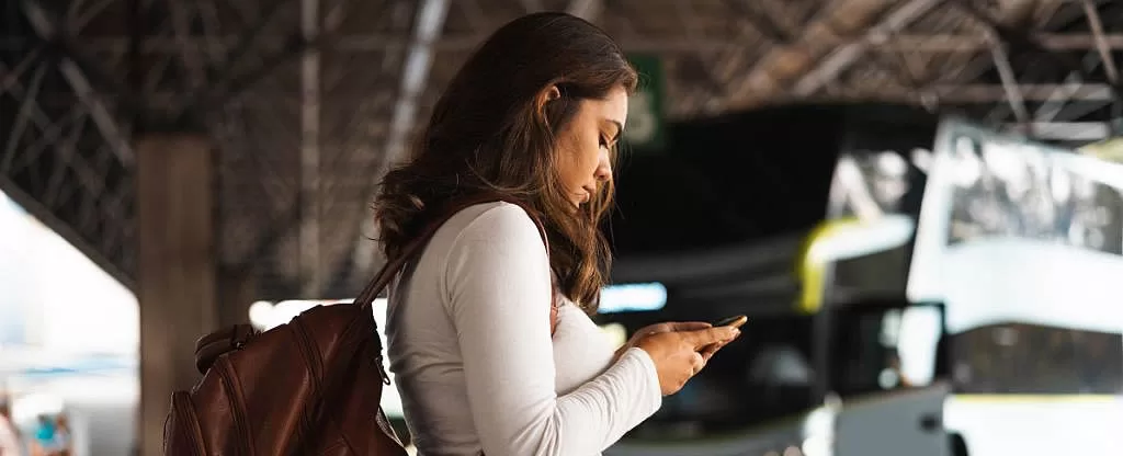Mulher de blusa branca com mochila olhando o celular