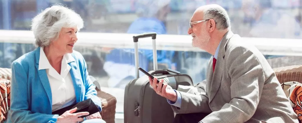 Homem e mulher idosos sentados próximos de uma mala - Acessibilidade em Viagem de ônibus