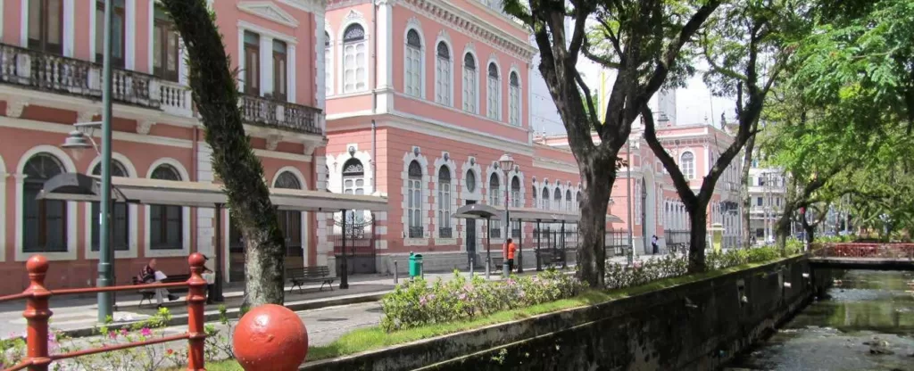 Petrópolis (RJ) Rua cortada por um canal com prédios em estilo colonial à esquerda e árvores à direita.