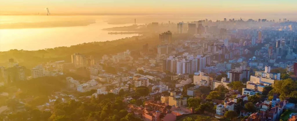 Porto Alegre (RS) Visão aérea ao entardecer com vários prédios à margem de um rio.