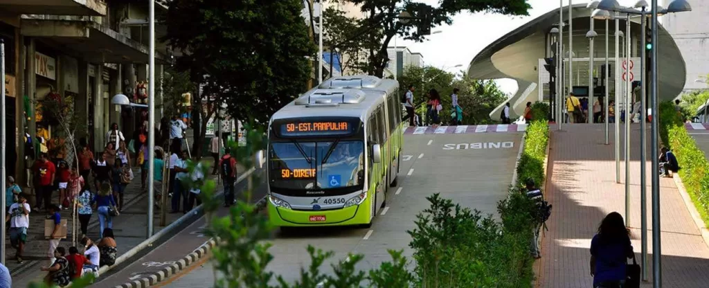 Belo Horizonte (MG) Ladeira com um ônibus descendo no meio da rua e pessoas andando na calçada em ambos os lados.