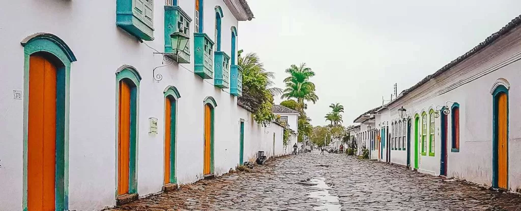 Rua de pedra cercada por casas antigas dos dois lados e coqueiros ao fundo.