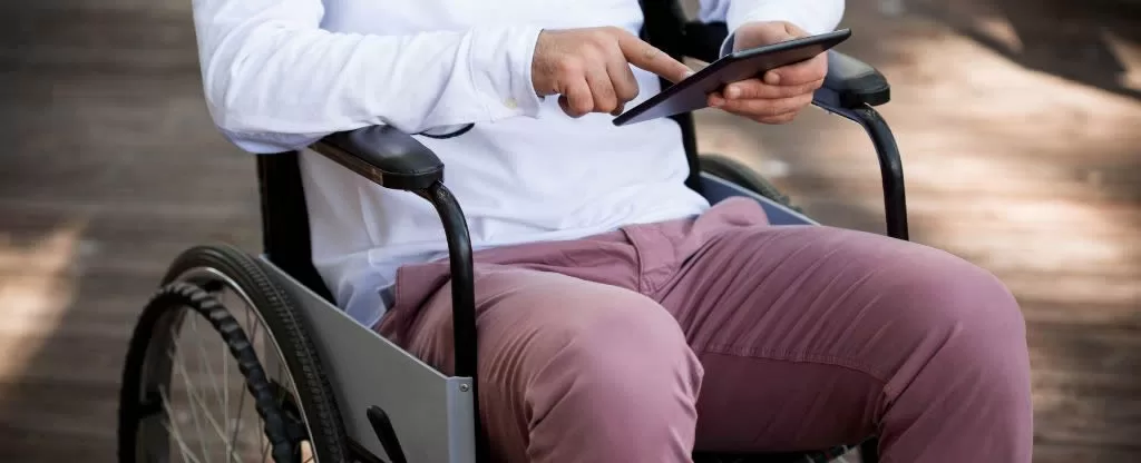 Homem sentado em uma cadeira de rodas mexendo em tablete
