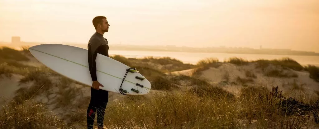Homem segurando prancha de surf olhando para o mar Homem segurando prancha de surf olhando para o mar