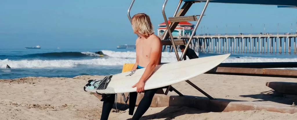 Homem sentado segurando prancha de surf e olhando para o mar Homem sentado segurando prancha de surf e olhando para o mar