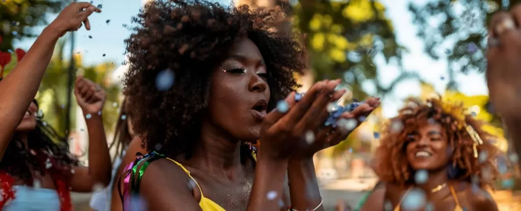 Mulher negra com cabelos curtos soprando confetes Mulher negra com cabelos curtos soprando confetes