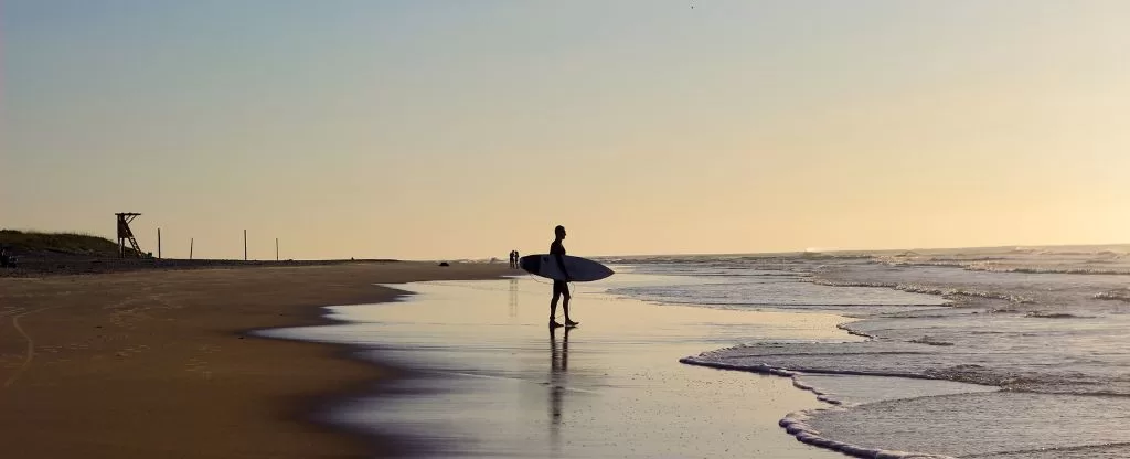 Homem com prancha de surf - Melhores praias para surfar em Florianópolis 